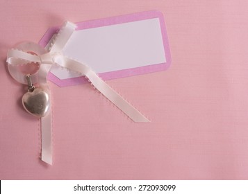 Above View of a Cute, Pink and White Notecard for a Baby Girl on Pink Cloth Background with room or space for copy, text, your words.  A Silver Heart shape Teething Ring. Horizontal looking down