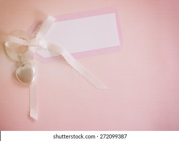 Above View Of A Cute, Pink And White Notecard For A Baby Girl On A Cloth Background With Room Or Space For Copy, Text, Your Words.  A Silver Heart Shape Teething Ring.  Horizontal Instagram Light.