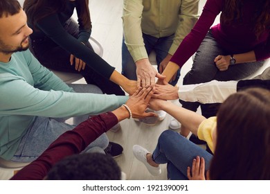 From above view of diverse senior and young people sitting in circle and putting hands together in community meeting or group therapy session. Concept of support, unity, success, help and trust