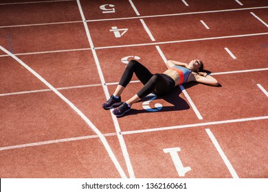 From Above View Of Exhausted Teen Athlete In Sportswear Resting On Track After Finishing Tough Race