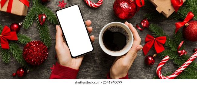 Above view of female hand holding smart phone with hot cup of coffee. Christmas decoration on colored background. - Powered by Shutterstock