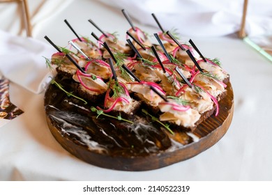 Above View Of Festive Appetizer On Wooden Tableware, Which Includes Toast Rounds, Fish And Decorated By Red Onion And Micro Greens, Located On Wedding Buffet 