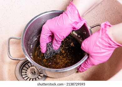 above view of gloved hands scrub stewpan with burnt food with metal sponge in pink sink at home kitchen - Shutterstock ID 2138729593