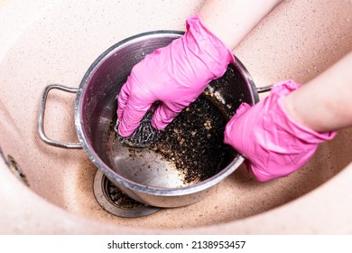 Above View Of Gloved Hands Wash Pan With Burnt Food With Metal Sponge In Pink Sink At Home Kitchen