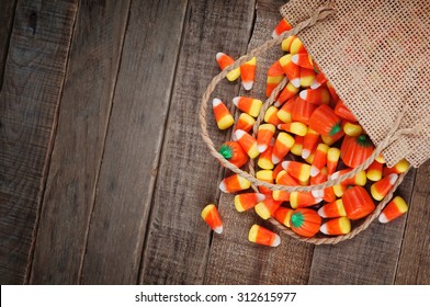 Above View Of Halloween Candy Corn Spilling From A Burlap Bag On Rustic Wood Board Background With Room Or Space For Copy, Text, Your Words.  Horizontal That Works Vertical With Moody, Dark Vignette