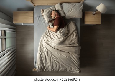 Above view of handsome middle aged man in pajamas resting at home, sleeping on his side in comfortable bed, copy space, full length shot