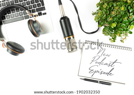 above view of laptop computer, microphone and notepad with text NEW PODCAST EPISODE on clean white desk, podcasting concept