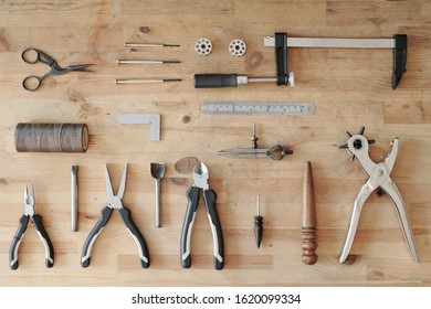 Above view of leather work tool set such as rotary punch, ruler, thread, pliers, edge burnisher on wooden table - Shutterstock ID 1620099334