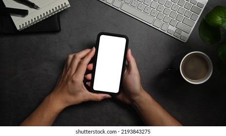 Above View Man Hands Holding Smart Phone Over Black Stone Table. White Empty Screen For Your Advertise Text