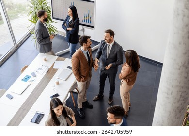 From above view of managers standing in groups in boardroom and taking a break from meeting.