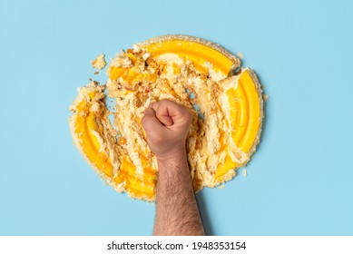 Above view with a man's fist smashing a cake. Concept for dieting with an orange whipped cream cake destroyed by a man, top view.
