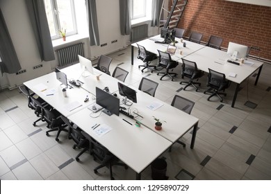 Above View Modern Spacious Office Interior. From Top Empty Room With Computers On Tables Black Chairs On Wheels, Daylight Through Windows. Comfortable Contemporary Coworking Space For Work No People