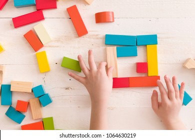 Above view on child's hands playing with wooden cubes on white wooden table background. 