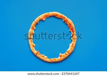 Above view with only the crust from a pizza, minimalist on a blue background. Pizza leftovers arranged in a circle on a blue table