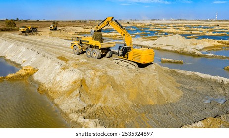 Above view over opencast surface sand mining, mine sand pit. Big excavator is excavating sand and loading into large, heavy duty dump truck. Area with subterranean waters