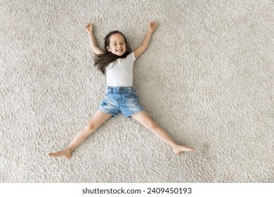 Above view playful beautiful little girl relaxing at home, spread her arms and legs lying on warm floor, looks carefree, feel happy, spend free time indoor, enjoy soft pile of new bought beige carpet - Powered by Shutterstock