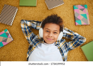 Above view portrait of teenage African boy wearing headphones and smiling at camera while lying on floor enjoying music, copy space - Powered by Shutterstock