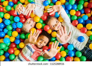 Above view portrait of three happy little kids in ball pit smiling at camera raising hands while having fun in children play center, copy space - Shutterstock ID 1125288926