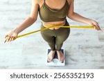 Above view of shocked Indian lady standing on scales, checking her waist measurements, surprised with unexpected results of weight loss program, indoors. Slimming diet and workout concept