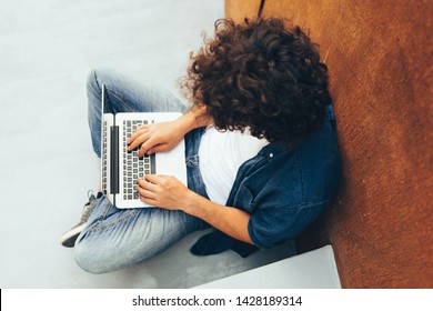 Above View Shot Of Man With Curly Hair Using Laptop For Chatting Online With Friends, Connected To Free Wireless On The City Street. Handsome Freelancer Man Sitting On Concrete Stairs With Laptop.