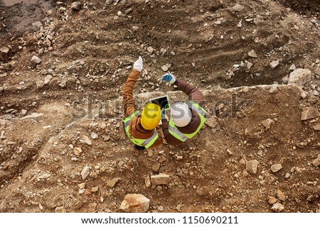 Above view shot of two industrial  workers wearing reflective jackets and hardhats standing on mining worksite outdoors using digital tablet, copy space