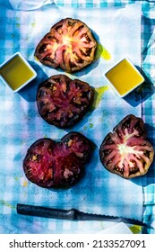 Above View Of Slices Of Black Heirloom Tomatoes On Parchment Paper Over Aqua Gingham Check Cloth