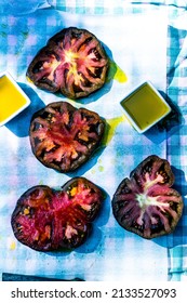 Above View Of Slices Of Black Heirloom Tomatoes On Parchment Paper Over Aqua Gingham Check Cloth