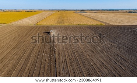 Above view, tractor pull disc harrow, harrowing farmland, preparing soil for next season, new crop. Flock of hungry white birds following, fly around agricultural machine in food search.