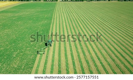 Above view, tractor is pulling grass cutting machine over field with clover, cutting alfalfa in straight lines, side swath mower.