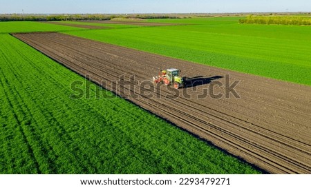 Above view, of tractor as pulling mechanical seeder machine over arable field, soil, planting new cereal crop, corn, maize.