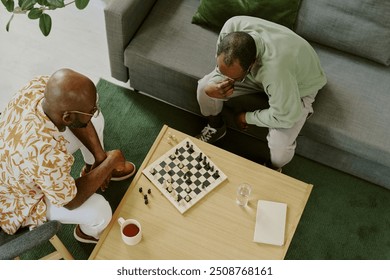 From above view of two young African American friends sitting in living room thinking over tactics while playing chess - Powered by Shutterstock