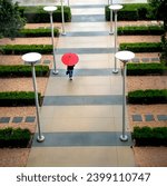 Above view of an unidentifiable businessperson walking on sidwalk with a red umbrella on a rainy day