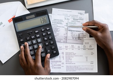 Above view of unrecognizable blackman checking receipts using calculator at table
