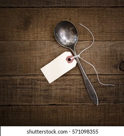 Above View of an Vintage Spoon with a Blank Off White Tag Tied with String centered on Textured, Distressed wood in a square crop with dark, moody vignette.  The card is for your words, text or copy