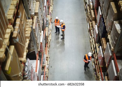 Above view of warehouse workers group in aisle between rows of tall shelves full of packed boxes and goods