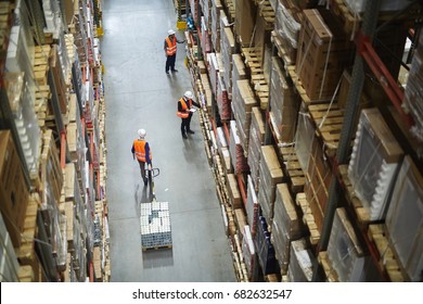 Above view of warehouse workers moving goods and counting stock in aisle between rows of tall shelves full of packed boxes