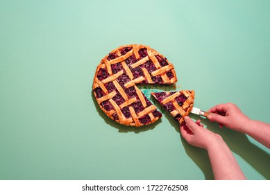 Above view with a woman's hands grabbing a slice of blueberries tart. Delicious homemade pie with a lattice crust and blueberries filling