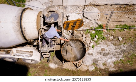Above view worker, driver as he standing on platform on mixer truck and washing ramp, canal, removing leftovers of fresh concrete after pouring, casting, cleaning remaining cement with water jet