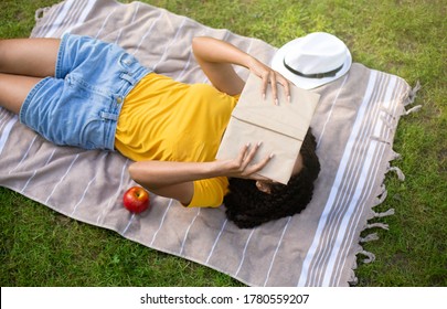 Above View Of Young Black Girl Reading Book On Picnic Blanket Outside