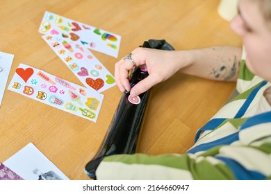 Above View Of Young Female With Physical Disability Putting Handmade Stickers On Her Myoelectric Arm While Sitting By Table