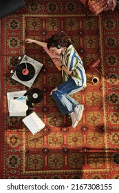 Above View Of Young Woman In Jeans And Shirt Looking At Record Player With Vynil Disk While Listening To Music In Headphones On The Floor