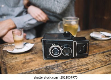 From Above Of Vintage Video Camera Placed On Wooden Table In Cafe With Anonymous Blurred Crop Couple Hugging On Background
