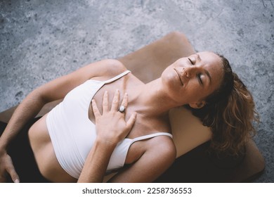 From above of young female with eyes closed lying on round cushion on floor while placing hands on lower abdomen and chest and inviting energy and peace during meditation - Shutterstock ID 2258736553