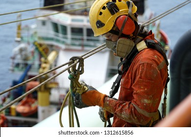 An Abseiler Wearing Personal Protective Equipment (PPE) Such As Respiratory Protection And Yellow Hard Hat Check The Condition Of Access Rope Knot Prior To Start Work.