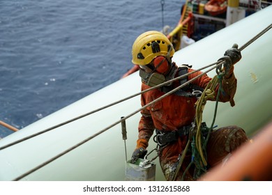 An Abseiler Wearing Personal Protective Equipment (PPE) Such As Respiratory Protection And Yellow Hard Hat Hanging In Between Pipeline For Painting Activities.