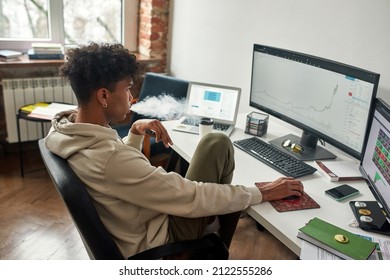 Absent-minded African American Broker Vaping While Watching Data Index Chart Stock Market. Worried Young Trader Working With Multiple Screens. Working From Home Concept.