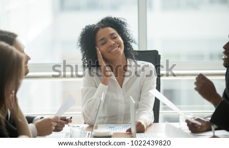 Absent-minded distracted black businesswoman dreaming of success and happiness at corporate group meeting, dreamy smiling african female boss thinking of new idea avoiding work stress lost in thought