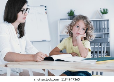 An absent-minded kid looking to the side and not at his homework notebook during a lesson with a tutor. - Powered by Shutterstock
