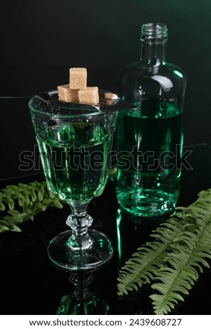 Absinthe, brown sugar, spoon and green leaves on mirror table. Alcoholic drink