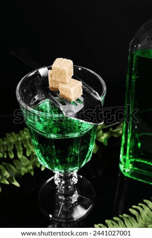 Absinthe in glass, brown sugar and spoon on mirror table, closeup. Alcoholic drink